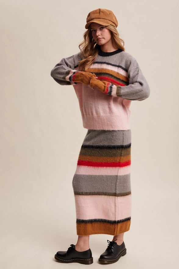 Woman wearing a colorful striped sweater and skirt with a beige cap on a plain background