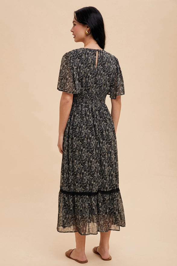 Woman wearing a black midi dress with flutter sleeves on a plain background