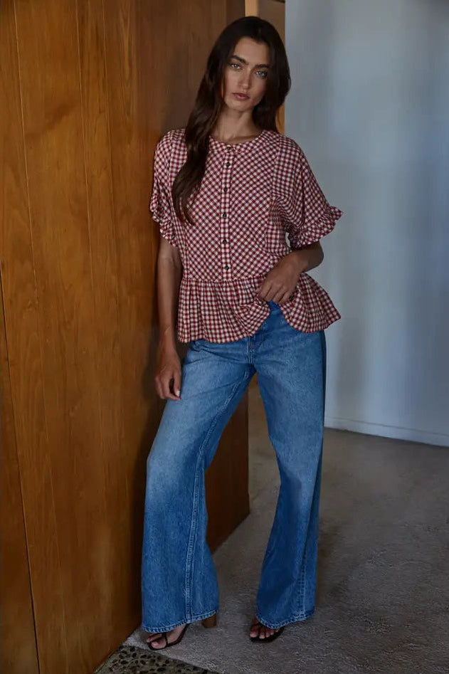 Woman wearing a checkered top and blue jeans standing against a wooden door.