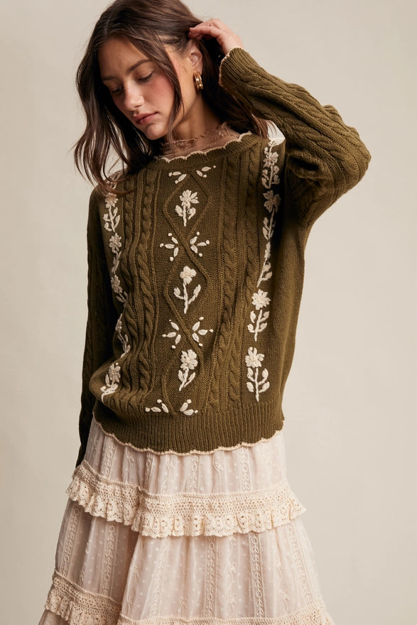 Woman wearing a green sweater with floral patterns and a white lace skirt on a beige background