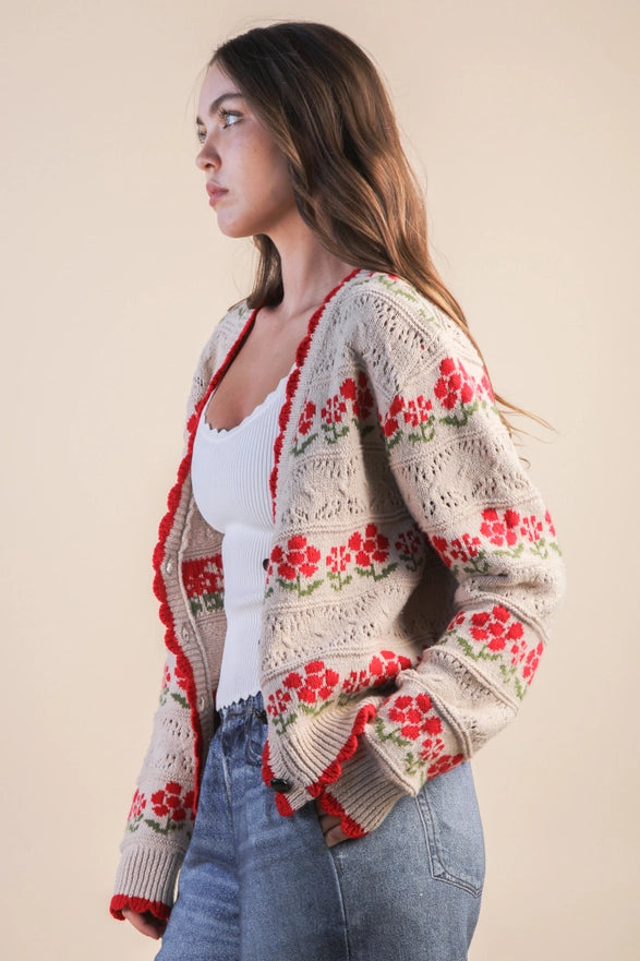 Woman wearing a floral crochet cardigan over a white top and blue jeans on a beige background