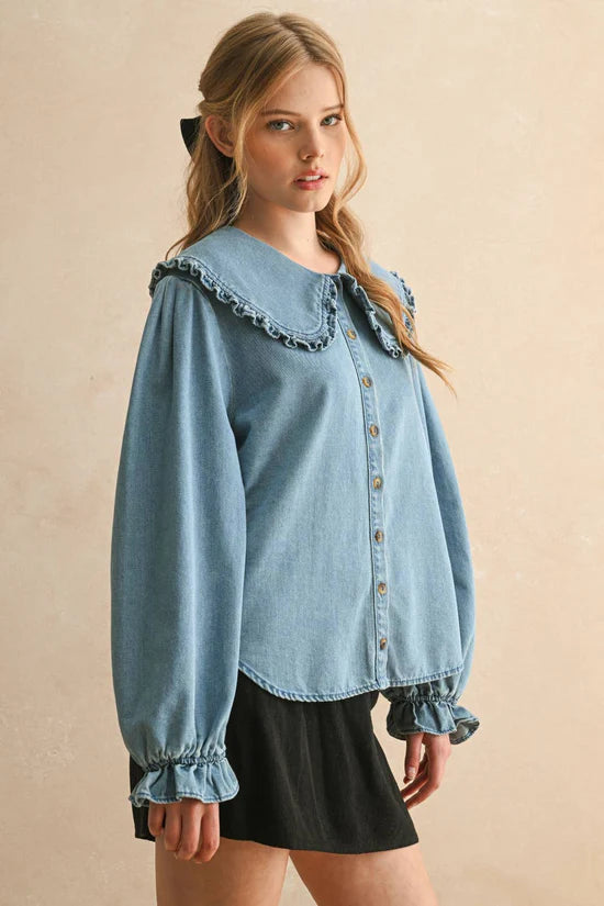 Woman wearing a light blue denim blouse with ruffled details on a beige background