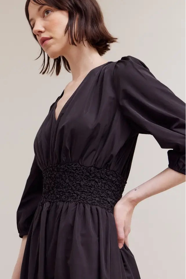 Woman wearing a black dress with a textured waistband on a plain background