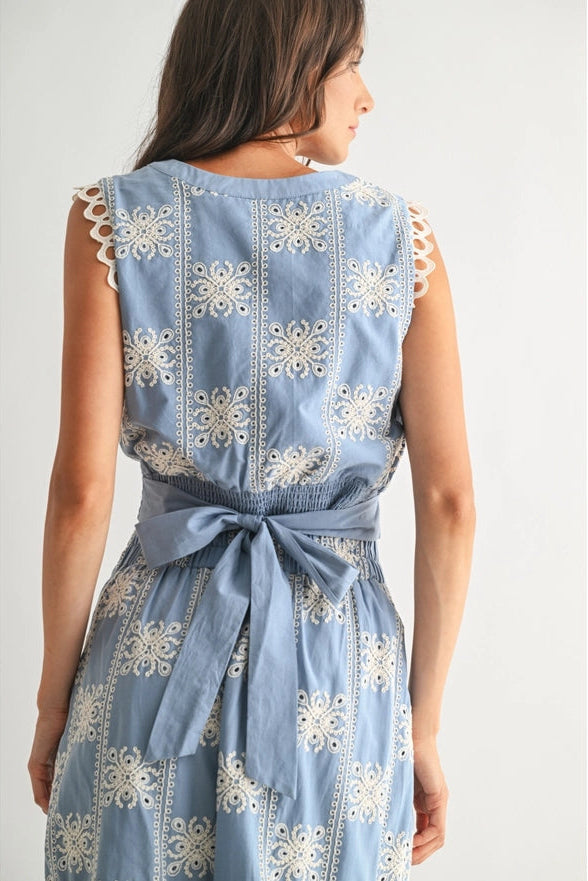 Woman wearing a blue dress with white floral embroidery on a plain background