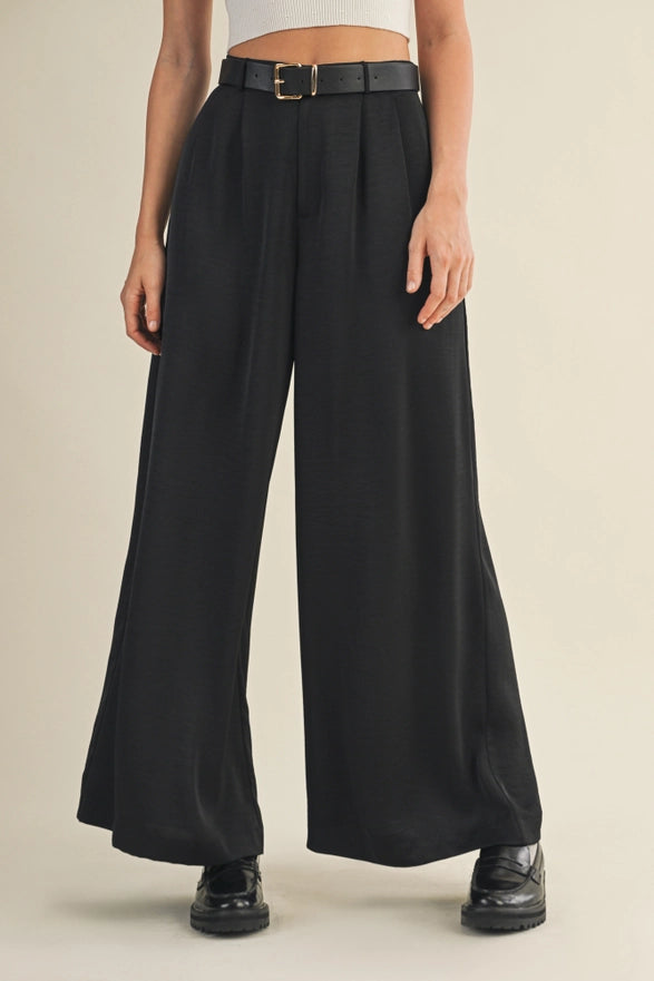 Person wearing black wide-leg pants with a belt on a beige background