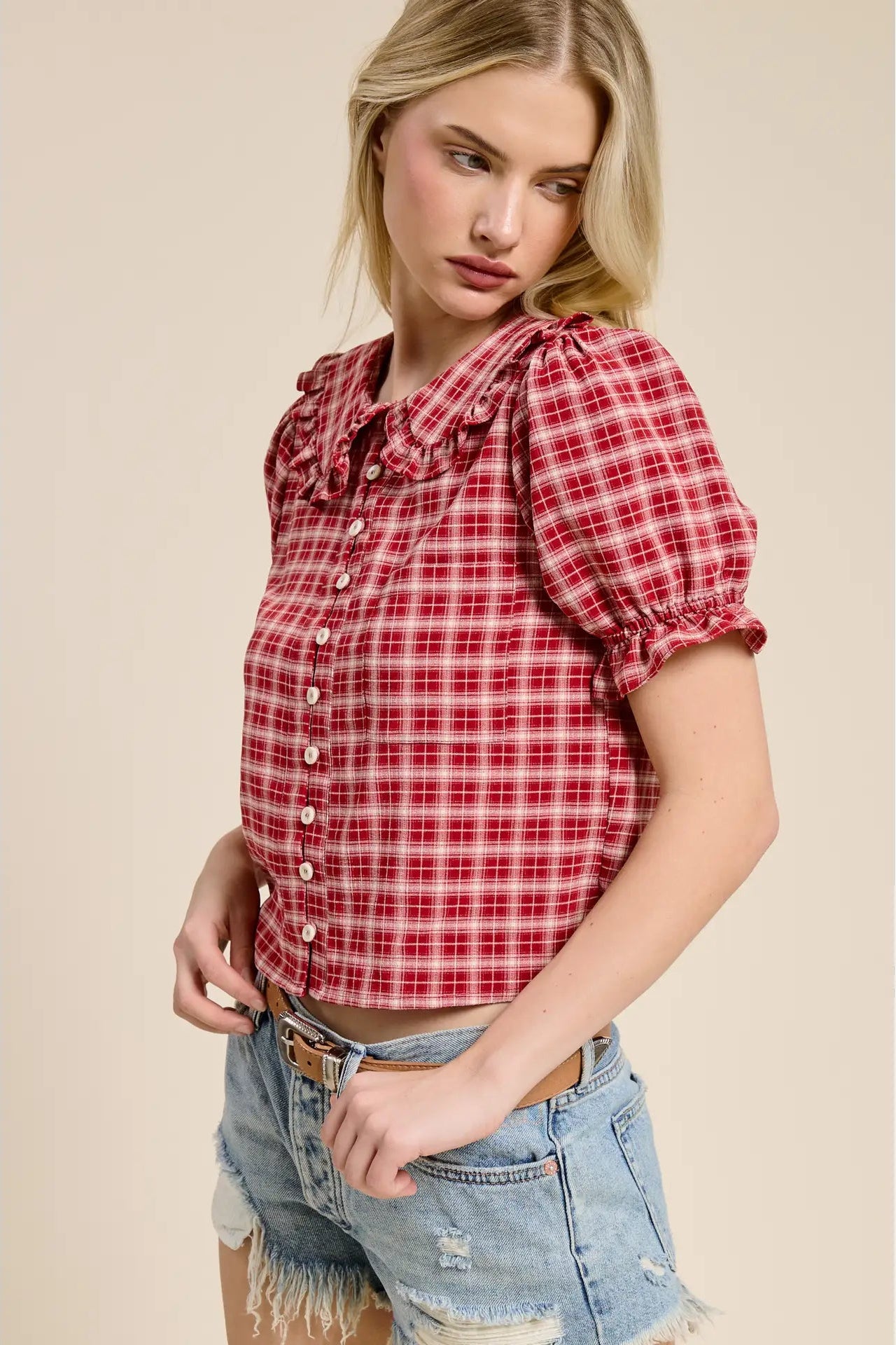 Woman wearing a red plaid shirt and denim shorts on a beige background