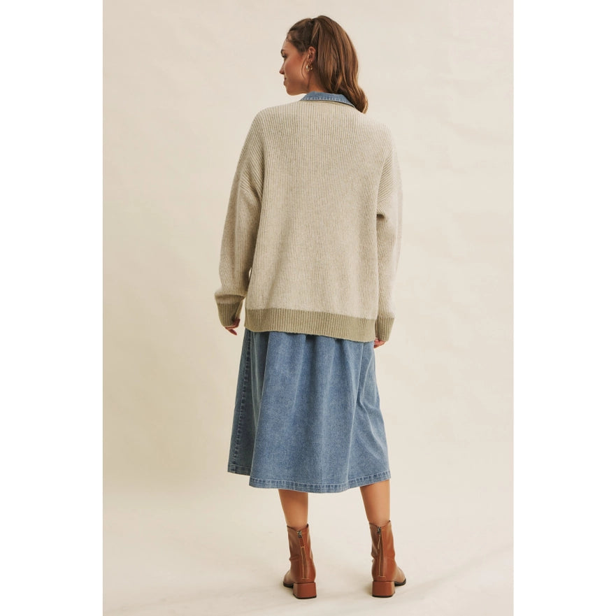 Woman wearing a beige sweater and blue denim skirt on a plain background