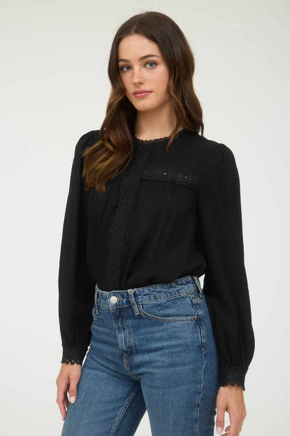 Woman wearing a black long-sleeve top and blue jeans against a white background