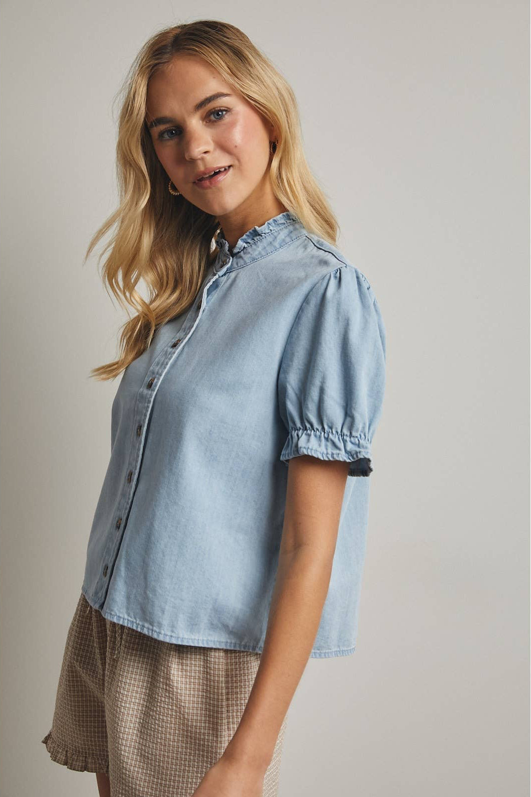 Woman wearing a light blue denim shirt against a plain background