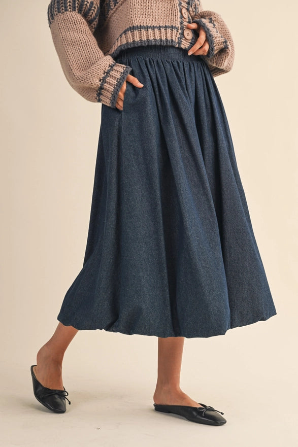 Person wearing a long navy skirt with a beige sweater on a beige background