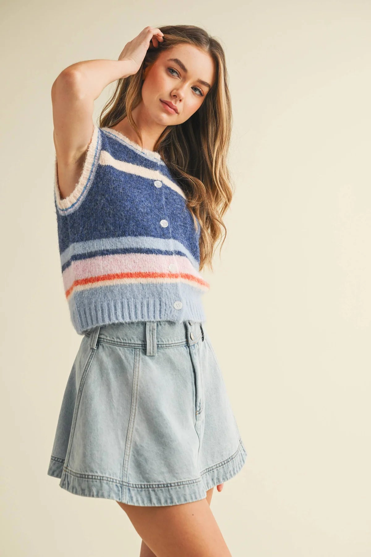 Woman wearing a striped sleeveless sweater and denim skirt on a beige background