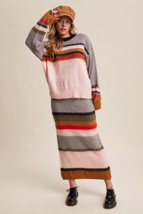 Woman wearing a long, multicolored striped sweater dress with a beige cap on a plain background