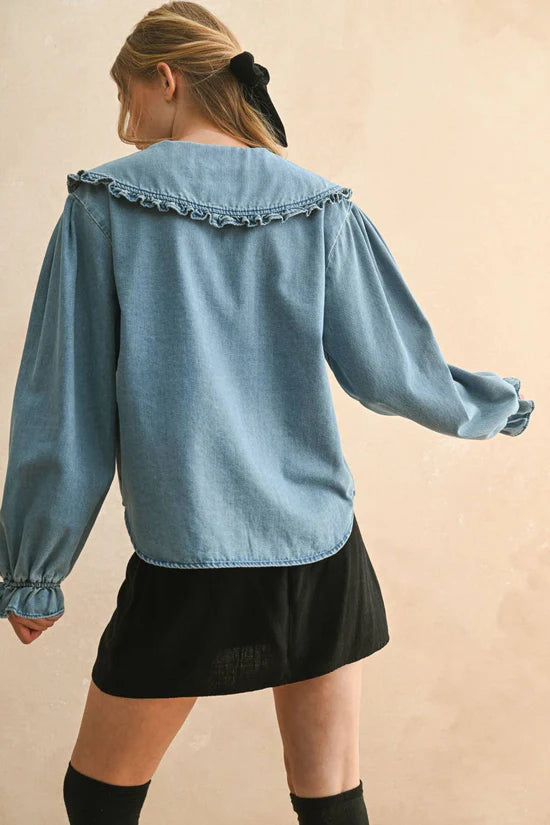 Person wearing a blue denim shirt with ruffled collar on a beige background