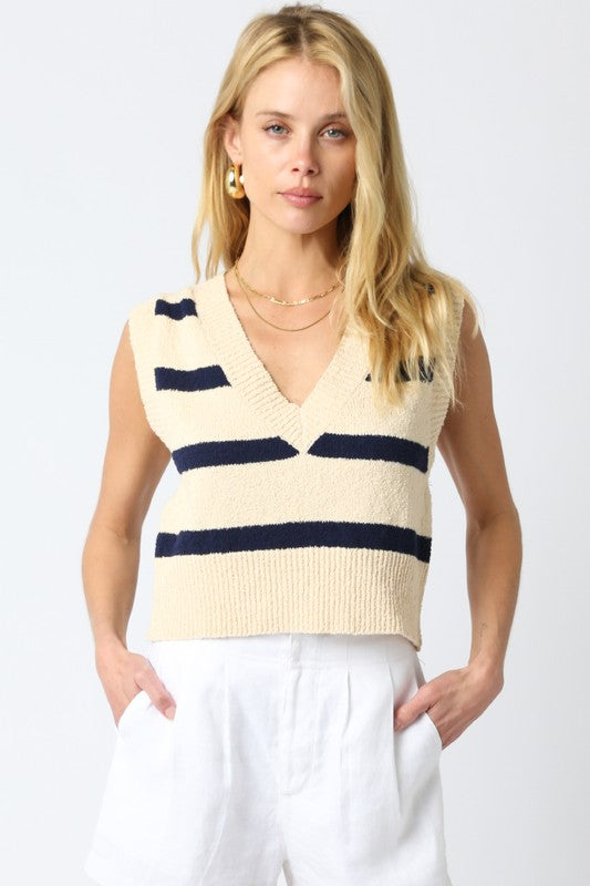 Woman wearing a cream-colored sleeveless sweater with navy stripes on a white background
