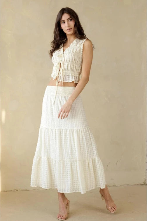 Woman wearing a white ruffled top and skirt set against a beige background