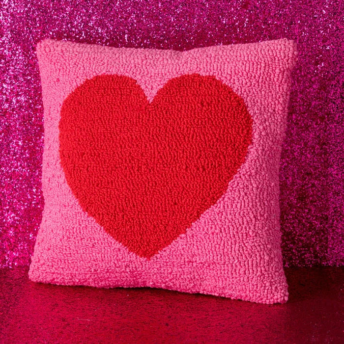 Pink pillow with a red heart design on a pink glittery background