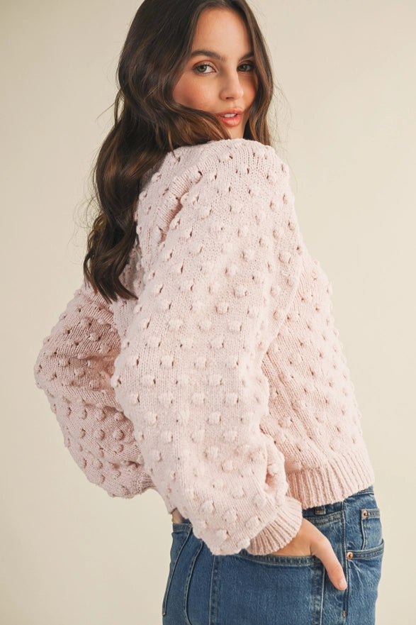 Woman wearing a light pink textured sweater and blue jeans against a plain background