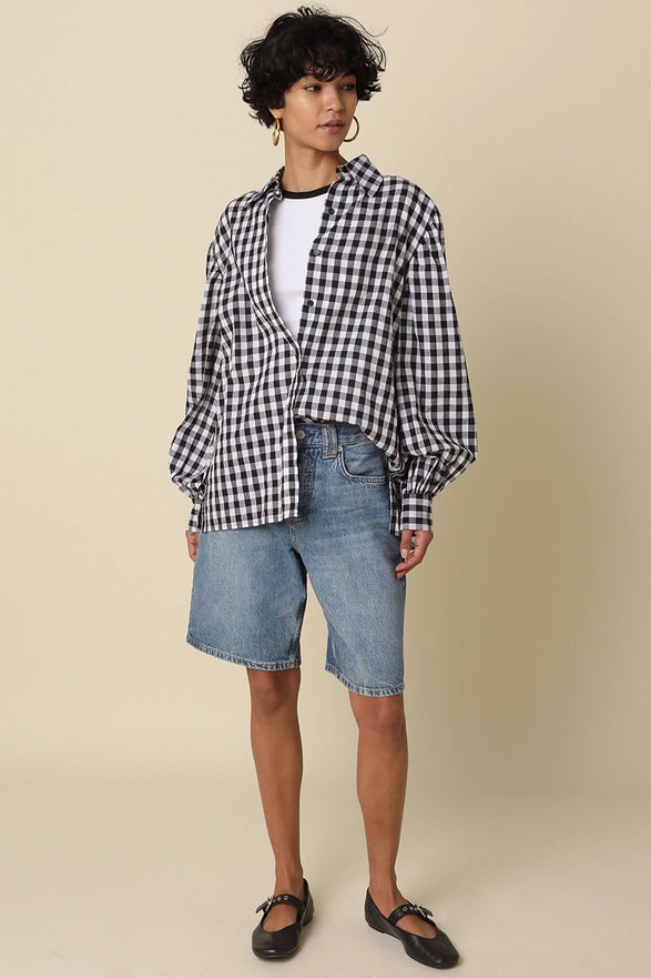 Person wearing a black and white checkered shirt with denim shorts on a beige background