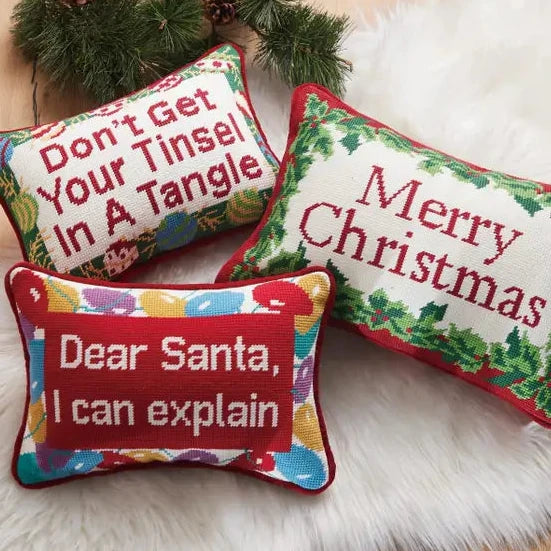 Three Christmas-themed pillows with humorous sayings on a white surface.