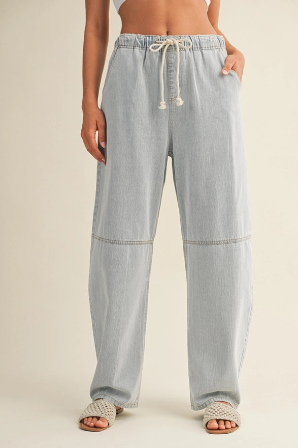 Light blue denim pants with drawstring waist on a beige background