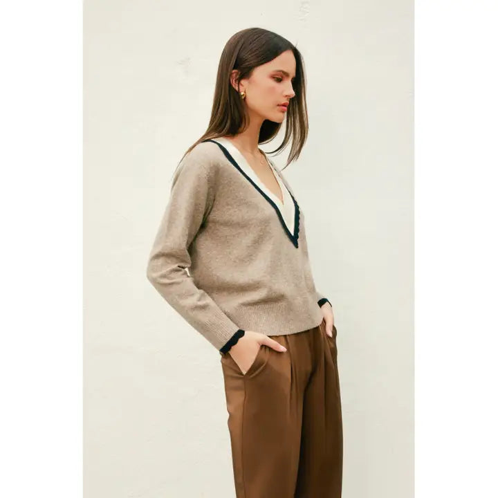 Woman wearing a beige sweater with a V-neck and brown pants on a light background