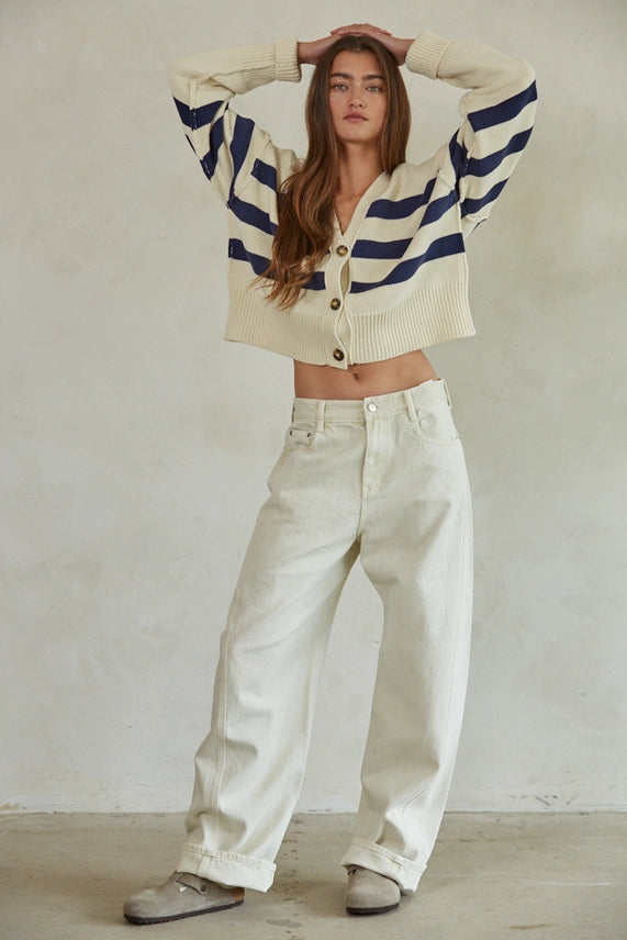 Woman wearing a striped sweater and white pants against a plain background