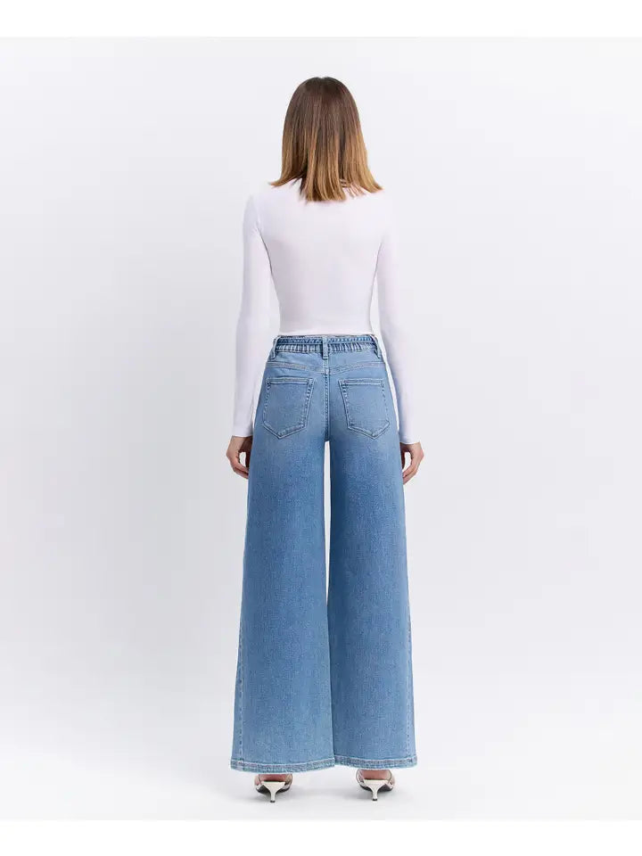 Woman wearing light blue wide-leg jeans and a white top on a white background