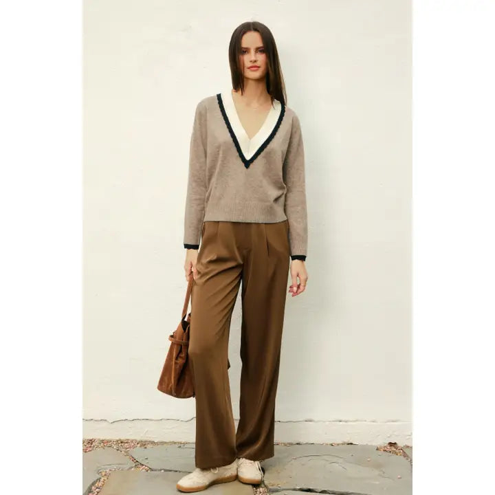 Woman wearing a brown sweater and pants holding a brown bag against a white background