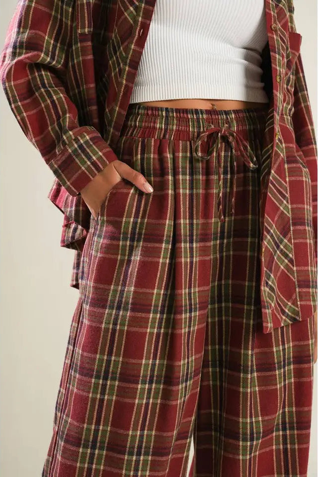 Person wearing a red plaid shirt and pants with a white top underneath on a plain background