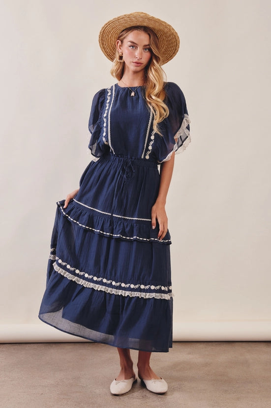 Woman wearing a navy blue dress with white trim and a straw hat against a plain background