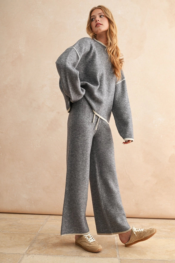 Woman wearing a gray outfit with wide-leg pants against a beige background