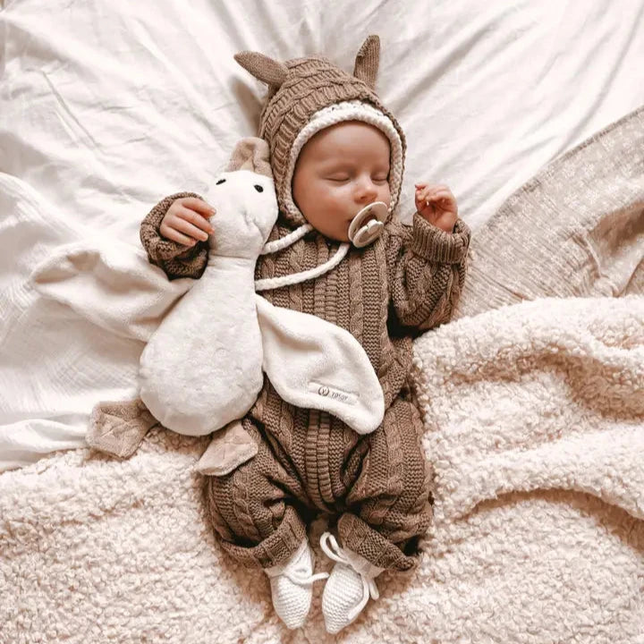 Baby in a brown dragon costume holding a white plush toy on a soft surface