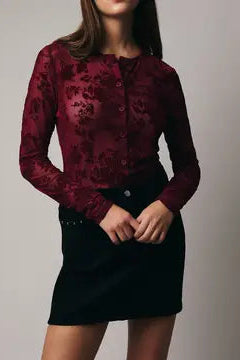 Woman wearing a burgundy floral blouse and black skirt against a plain background