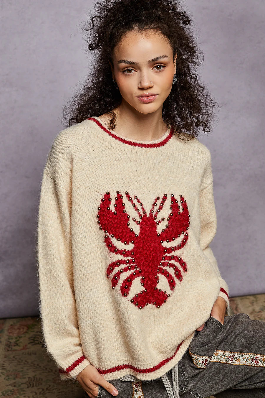 Person wearing a cream sweater with a red lobster design against a gray background