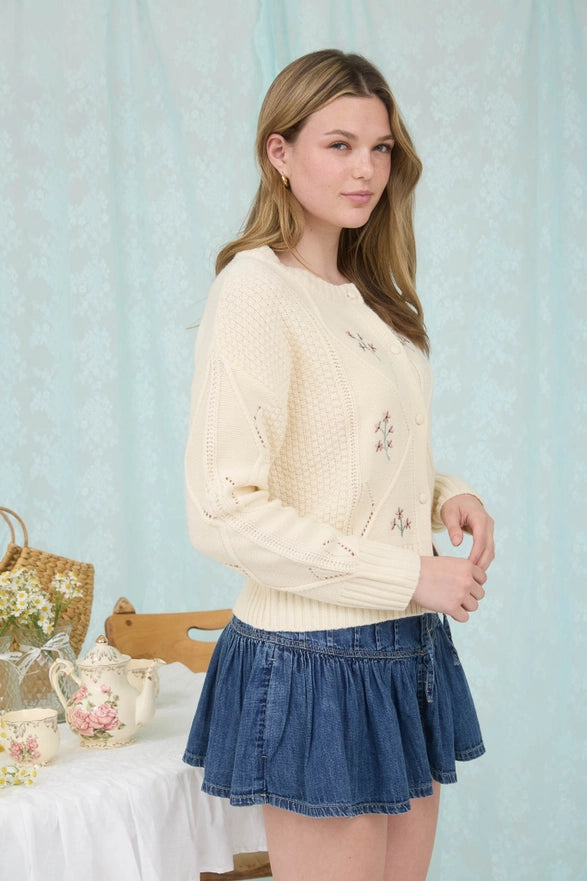 Woman wearing a cream sweater and blue skirt in a light blue room.