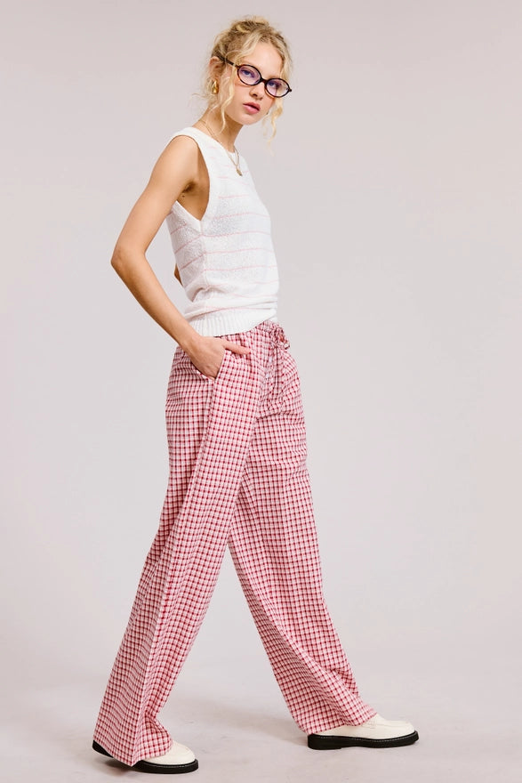 Woman wearing a white sleeveless top and red checkered pants on a plain background