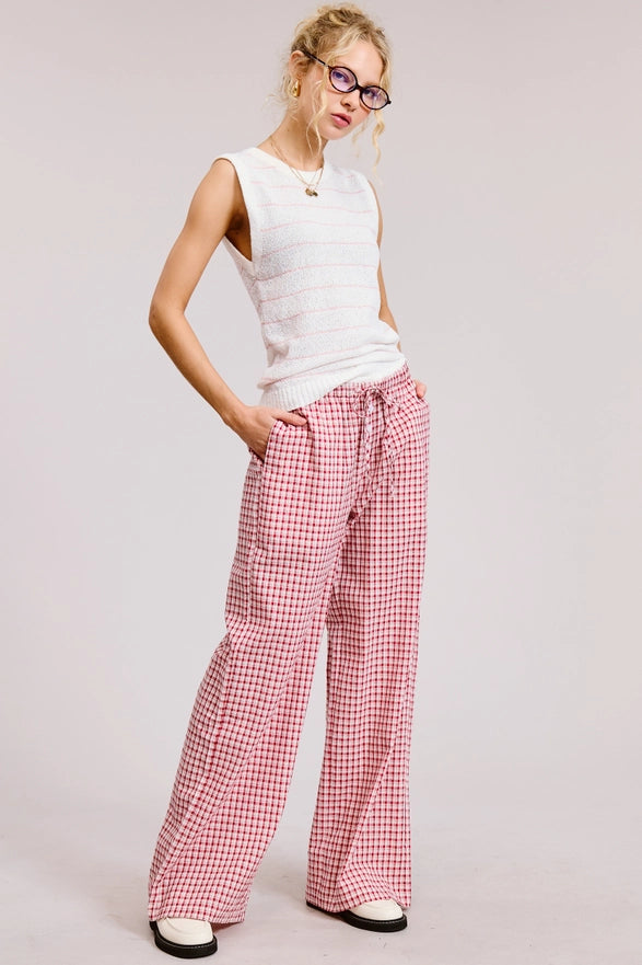 Woman wearing a white sleeveless top and red checkered pants on a plain background