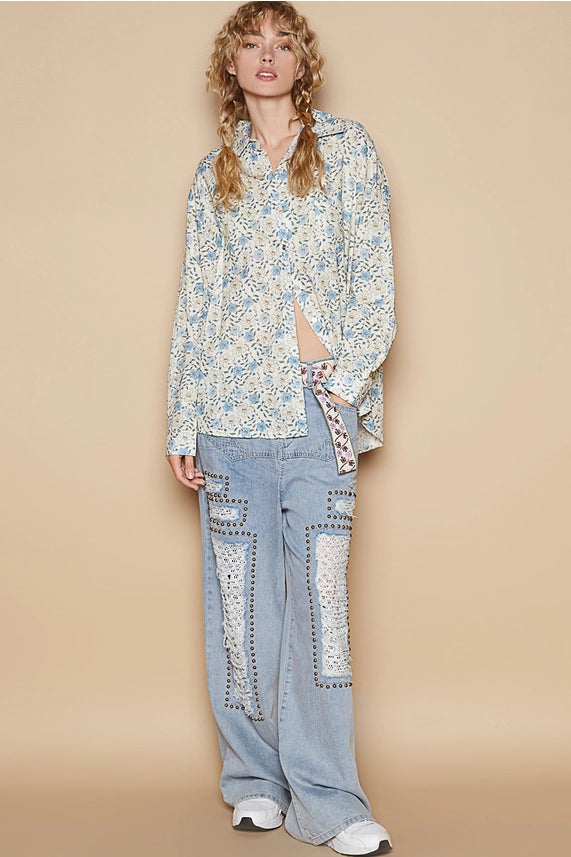 Woman wearing a floral blouse and light blue pants with white patterns on a beige background