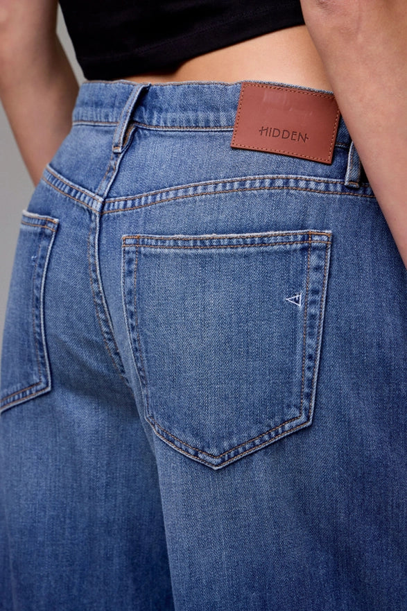 Blue jeans with a brown leather patch on the back pocket, featuring the brand 'Hidden'.