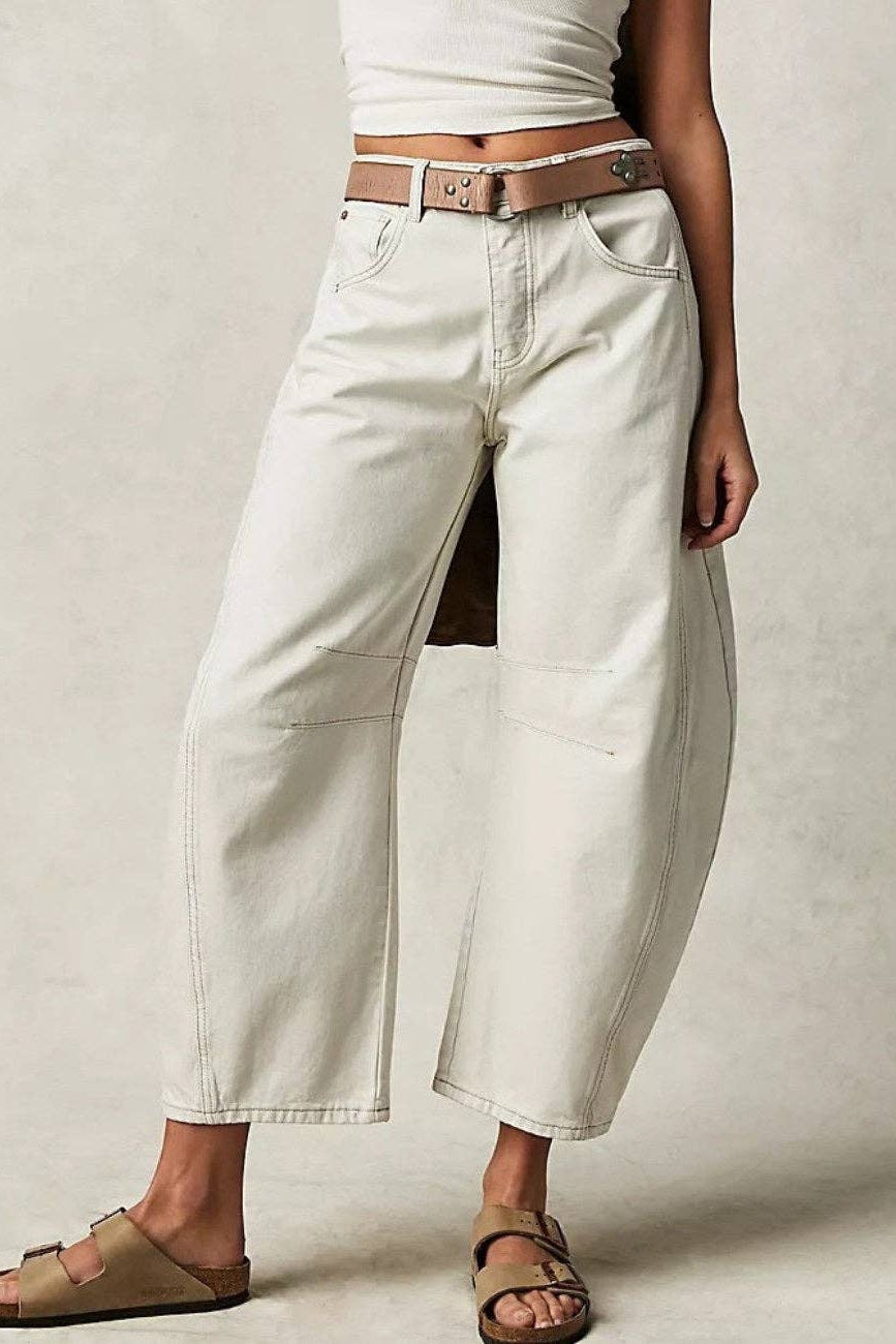Person wearing white wide-leg jeans with a brown belt on a plain background