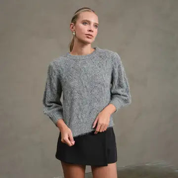 Woman wearing a gray sweater and black skirt against a plain background