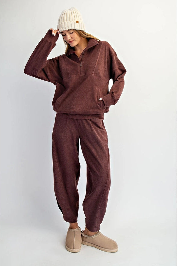 Person wearing a brown tracksuit and beige beanie on a white background