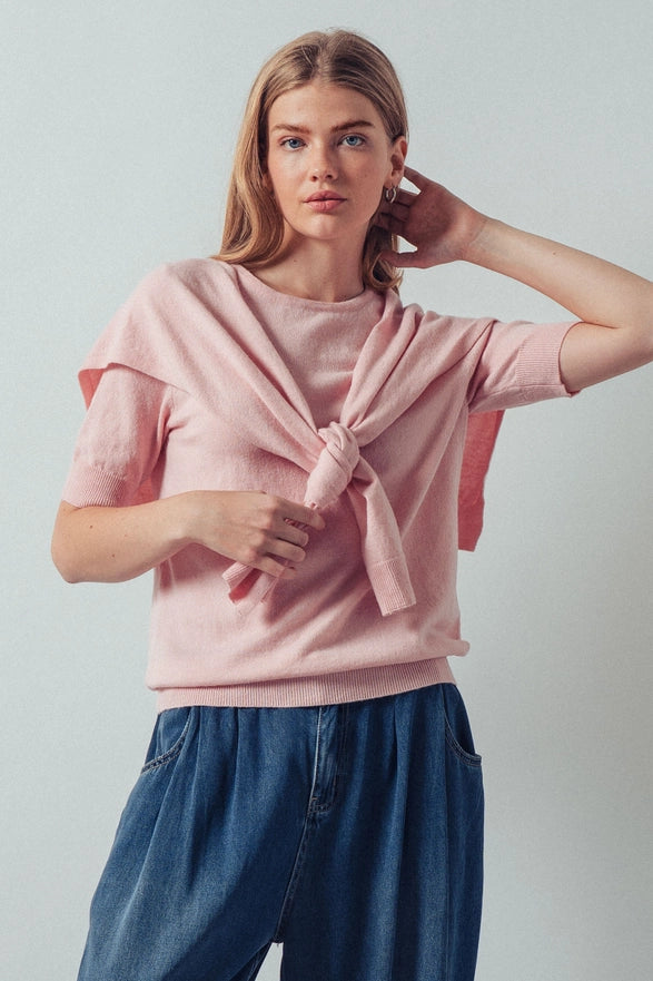 Woman wearing a pink knotted top and blue pants against a plain background