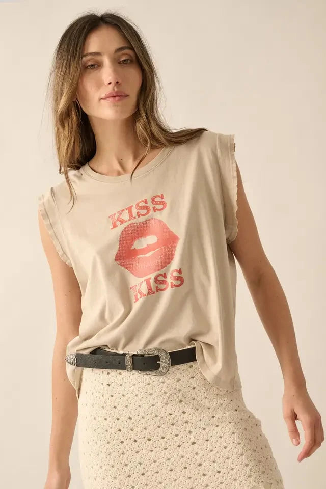 A woman wearing a beige graphic t-shirt with 'KISS KISS' text print and round neckline, paired with a dotted skirt and a black belt.