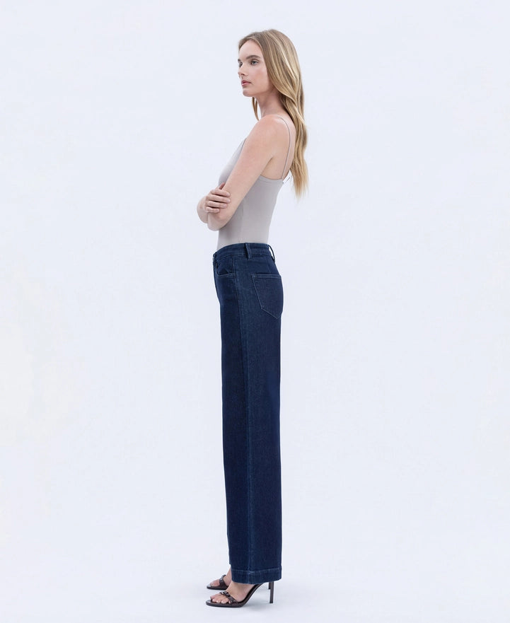 Woman wearing a light gray sleeveless top and dark blue jeans on a white background