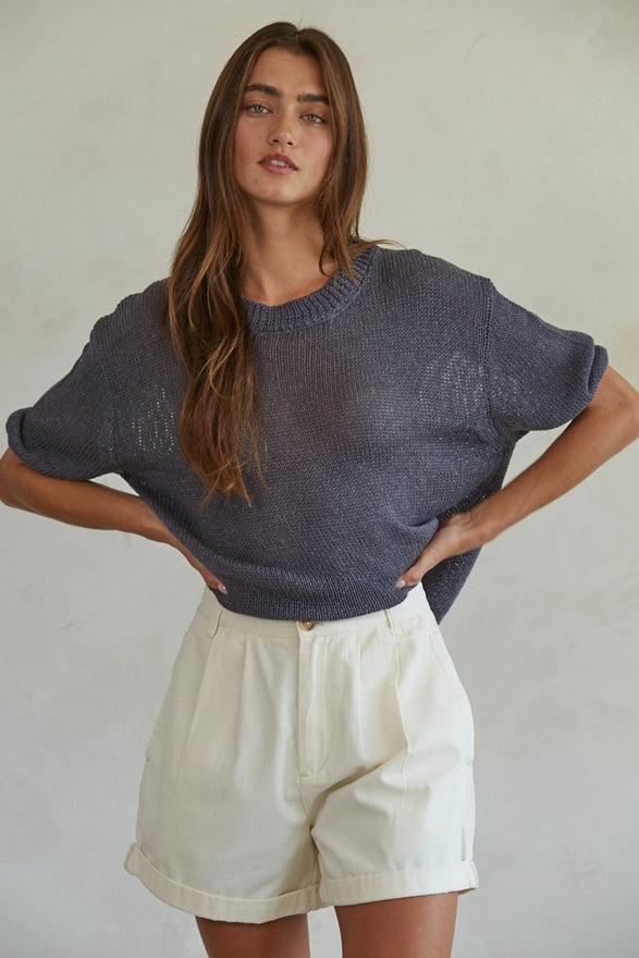 Woman wearing a blue sweater and white shorts against a neutral background