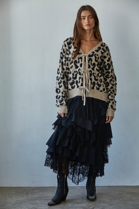 Woman wearing a leopard print sweater and black ruffled skirt against a plain background