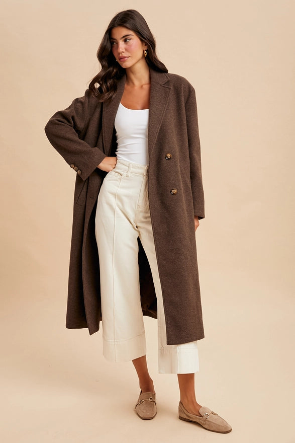 Woman wearing a brown coat over a white top and cream pants on a beige background