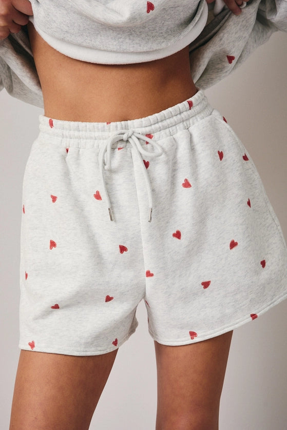 White shorts with red heart patterns worn by a person on a neutral background