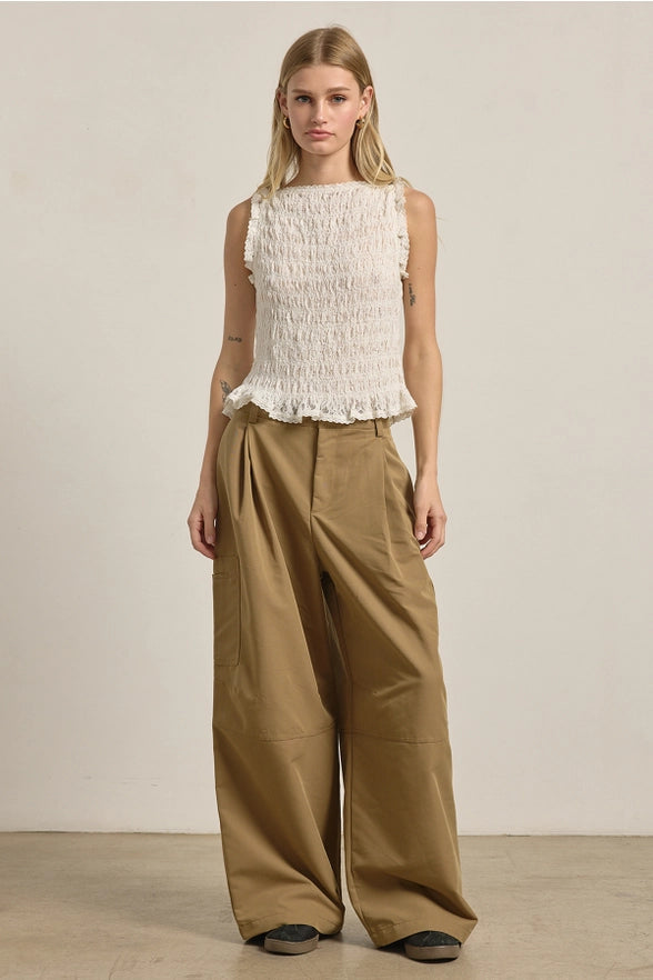 Woman wearing a white sleeveless top and brown wide-leg pants against a plain background